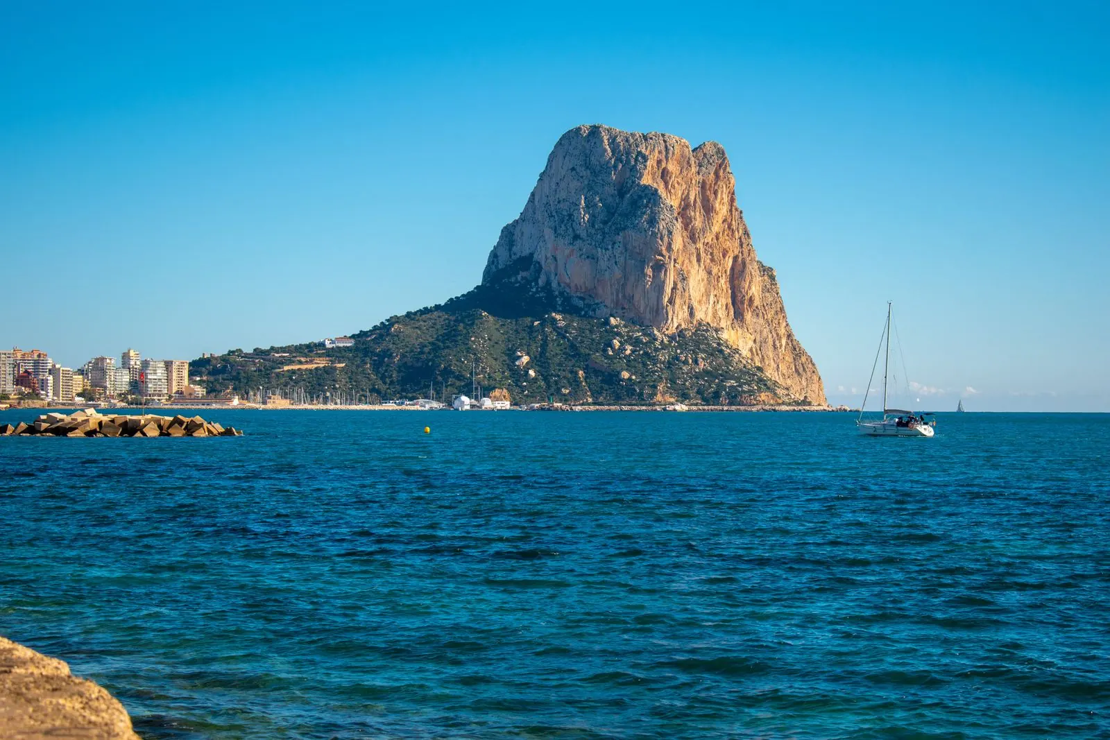 The Peñón de Ifach rock rising from a deep blue sea at Calp, with a sailing boat and the town behind